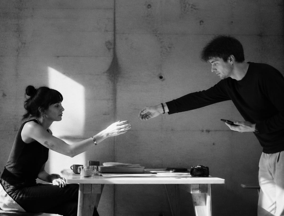 Two young creatives passing something across a concrete studio table